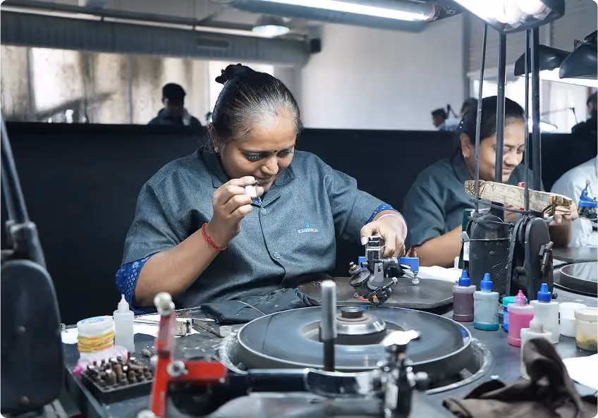An artisan using a loupe to inspect a stone beside a polishing wheel