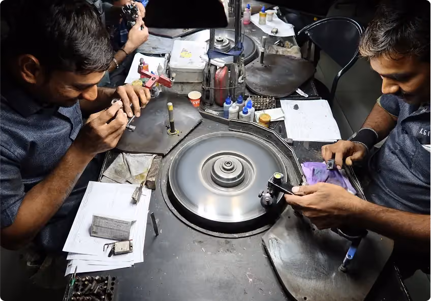 Two artisans inspecting and polishing stones at a shared polishing wheel