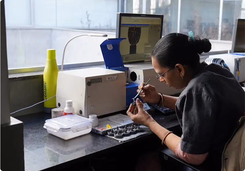 An artisan handling a stone beside inspection equipment and a monitor